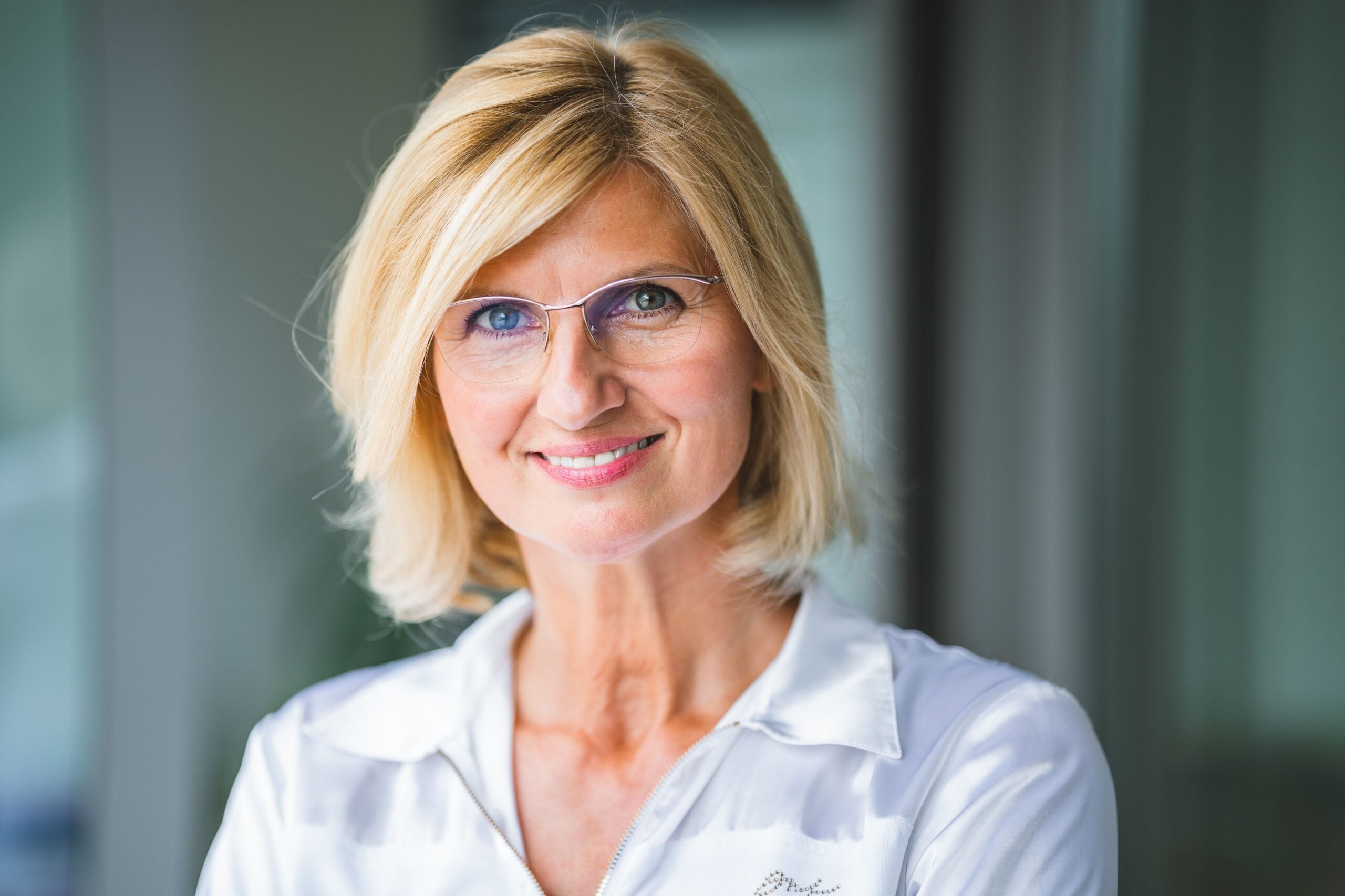 Close-up of a smiling blonde woman wearing eyeglasses indoors.